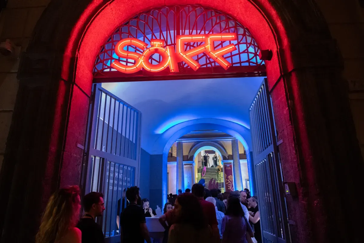 Il portale ad arco illuminato di rosso con la scritta SàFF al neon, e oltre la soglia un corridoio a colonne illuminato di blu