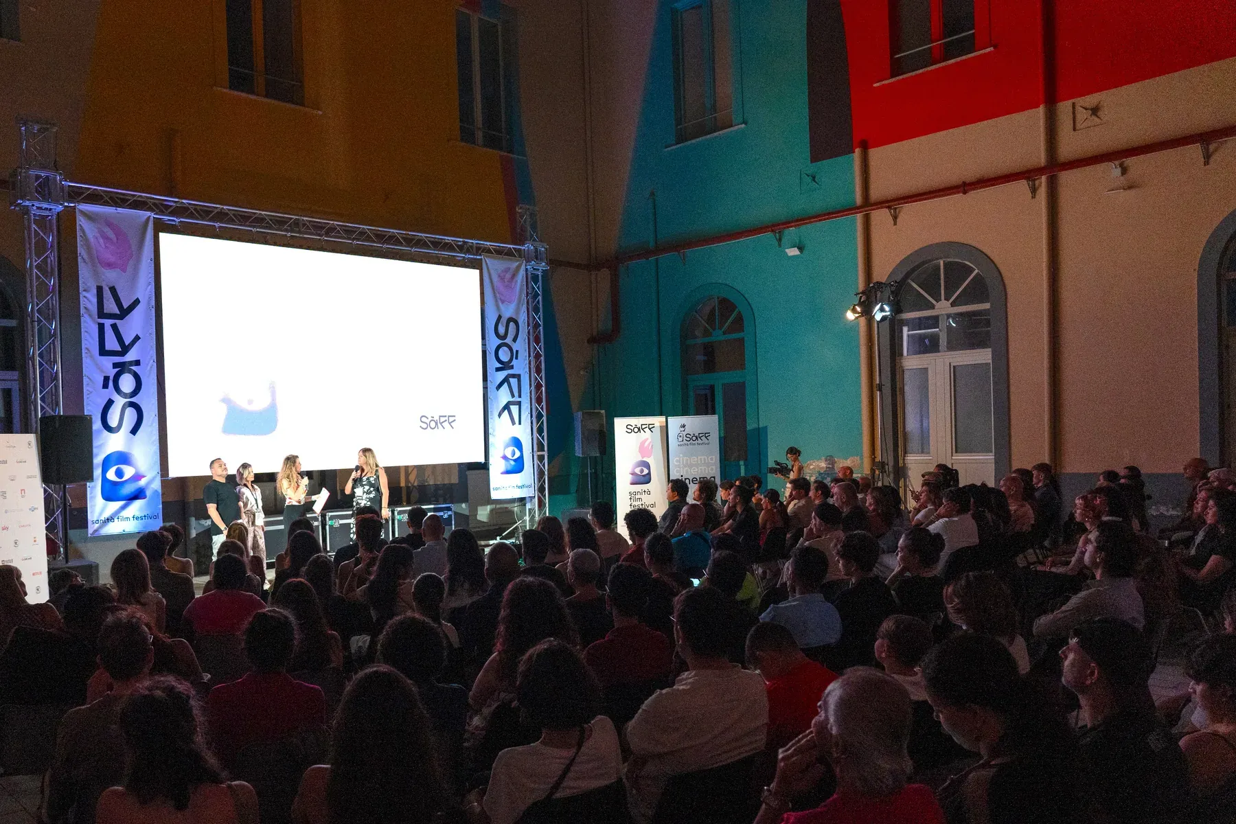 The audience seated in front of the large screen in the courtyard during an evening screening